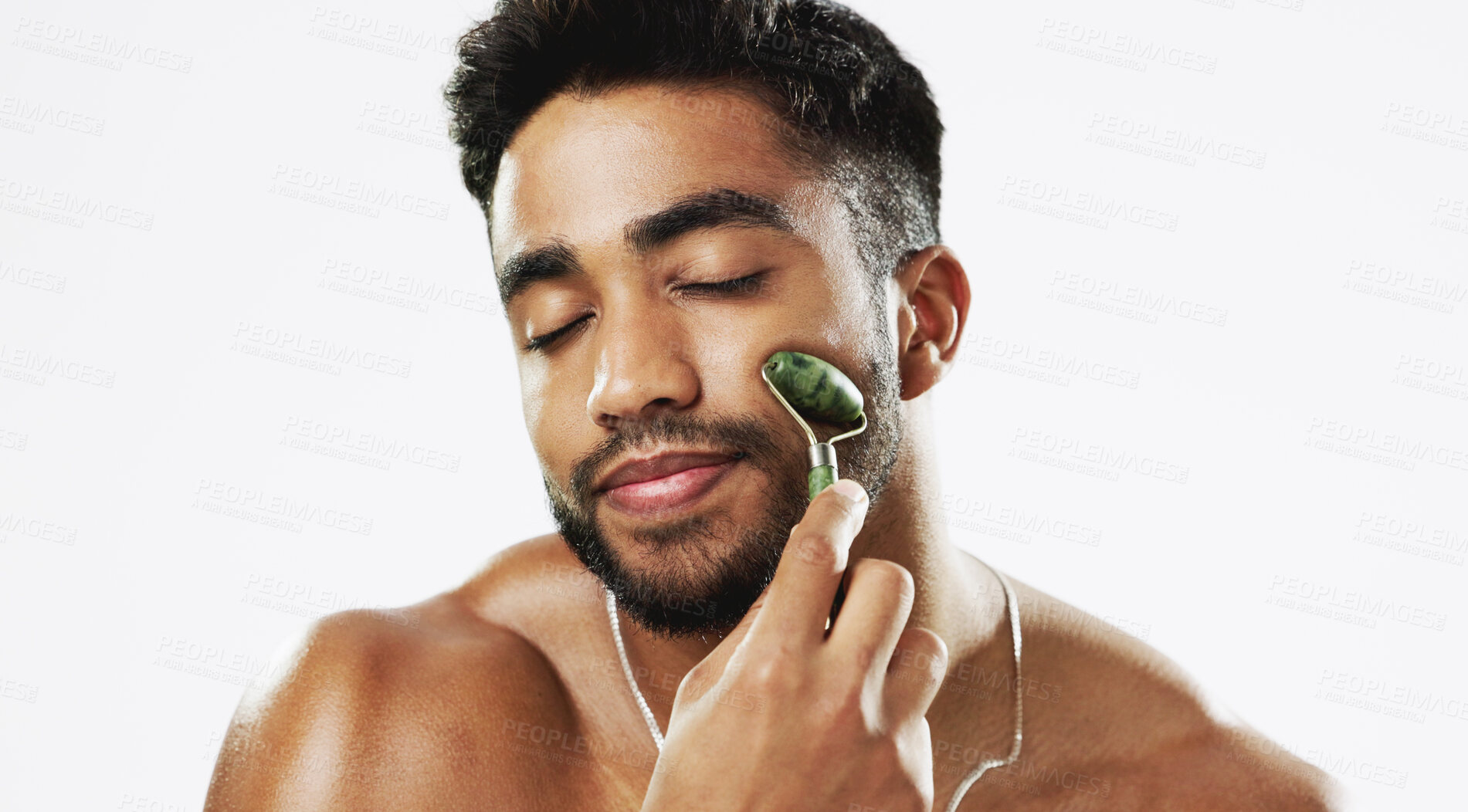 Buy stock photo Man, face and roller for beauty, skincare and benefits of aesthetic cosmetics in studio on white background. Indian model, jade crystal and facial massage for dermatology, lymphatic drainage and glow