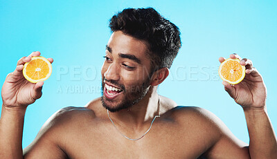 Skincare, orange and face of man in studio for beauty, wellness and citrus treatment on blue background. Fruit, facial and portrait of indian male model excited for organic vitamin c skin cosmetics