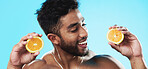 Orange, skincare and face of man in studio for beauty, wellness and citrus treatment on blue background. Fruit, facial and portrait of indian male model excited for organic vitamin c skin cosmetics