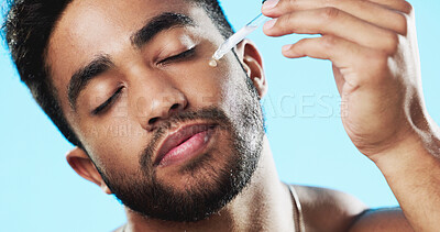 Skincare, health and man with face serum in a studio with a beauty, grooming and face routine. Wellness, cosmetic and male model with a facial oil pipette for a skin treatment by a blue background.