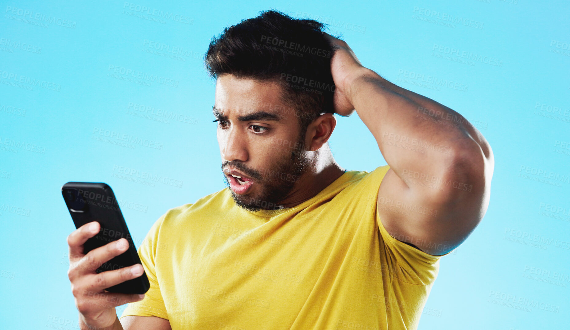 Buy stock photo Phone, shock and young man in studio reading post on social media with negative or bad news. Confused, cellphone and Indian male model with wtf, wow or omg face expression isolated by blue background