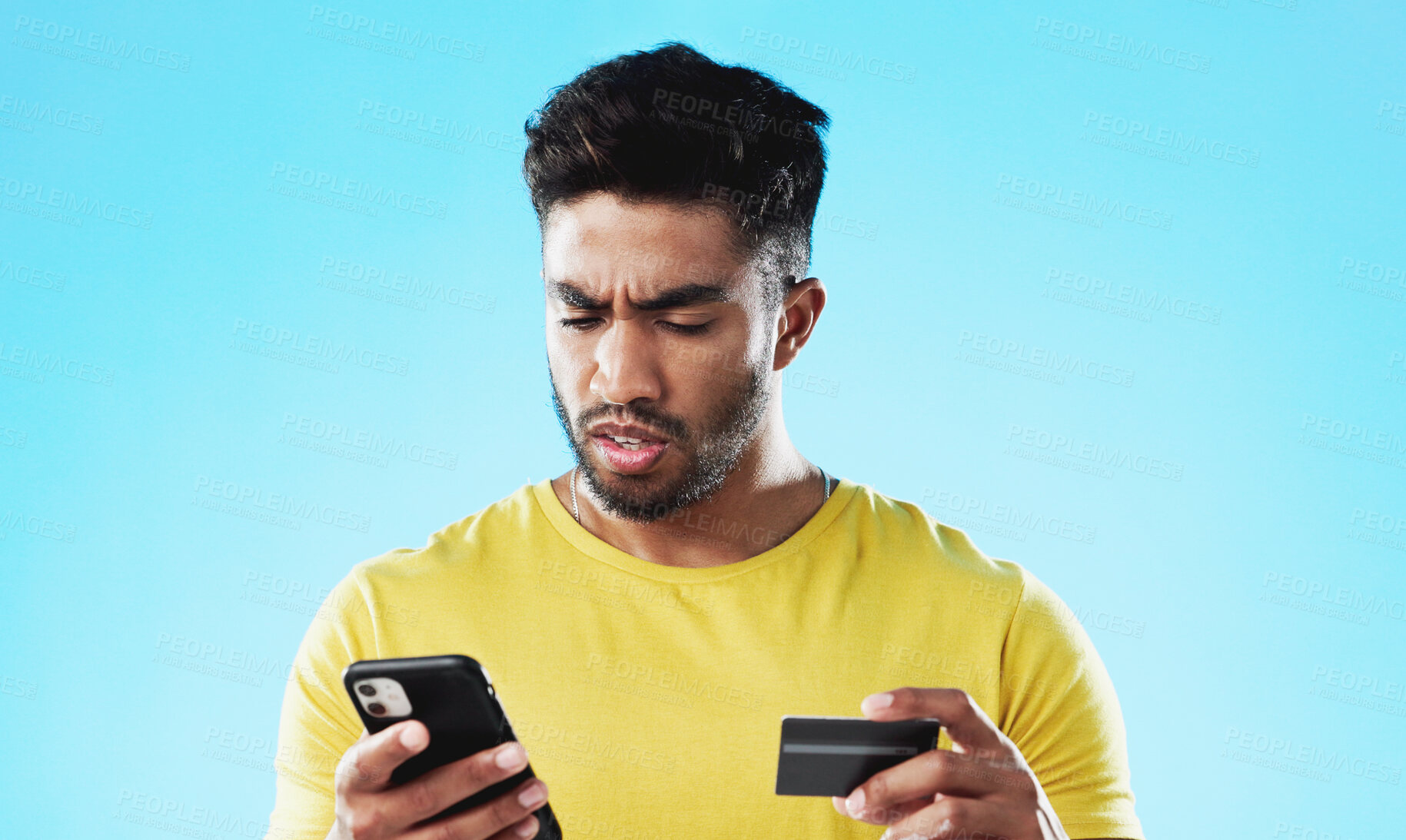 Buy stock photo Phone, credit card and frustrated broke man on a blue background in studio for retail. Ecommerce, fintech and debt with a confused young consumer using a mobile in a financial crisis or recession