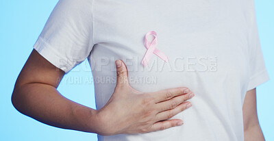 Pink ribbon, breast cancer and awareness with a woman in studio on a blue background for health. Chest, medical and healthcare with a female placing a bow, symbol or sign of recognition in october