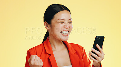 Winner, success celebration and Asian woman with phone in studio isolated on a yellow background. Surprise, fist pump or happy female with mobile to celebrate after winning lottery prize or good news
