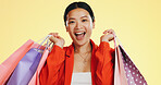 Happy, face and woman in studio with shopping, bag and boutique sale on yellow background. Portrait, excited and asian girl shopper customer with items for discount, fun and retail while isolated