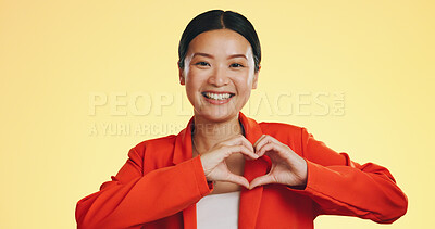 Smile, heart in hands and face of Asian woman on yellow background for love, support and charity mockup. Emoji, hand gesture and portrait of happy girl in studio with shape for care, trust and kind