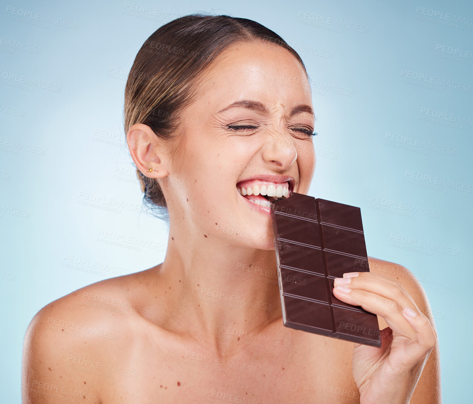 Buy stock photo Skincare, beauty and woman with chocolate in a studio for a health, wellness and facial treatment. Cosmetics, diet and girl model eating sweet cacao candy while doing skin routine by blue background.
