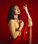 Portrait, confident and Indian woman with fashion, traditional dress and beauty against a red studio background. Face, female person or model with cultural clothes, jewellery and proud with aesthetic
