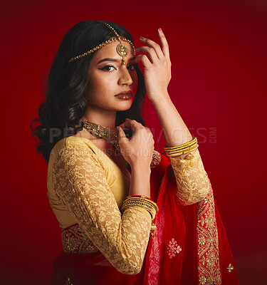 Buy stock photo Portrait, celebration and Indian woman with fashion, traditional dress and jewellery against a red studio background. Face, female person or model with cultural clothes, religion and beauty with gold
