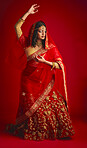 Fashion, dancing and Indian woman in a traditional dress, celebration and confident on a red studio background. Female person, girl and model with a cultural outfit, dancer and ritual with confidence