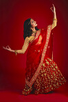 Fashion, dancer and Indian woman in a traditional dress, beauty and celebration on a red studio background. Female person, girl and model with a cultural outfit, dancing and confidence with religion