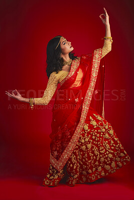 Buy stock photo Fashion, dancer and Indian woman in a traditional dress, beauty and celebration on a red studio background. Female person, girl and model with a cultural outfit, dancing and confidence with religion