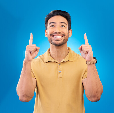 Buy stock photo Smile, casual and Asian man pointing up, promotion and opportunity against a blue studio background. Male person, guy or model with happiness, mockup space or direction with choice, happy or decision