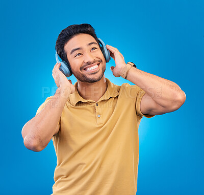 Buy stock photo Listening, music and asian man with smile or headphones in blue background in studio with streaming. Happiness, song and tech with guy or podcast for entertainment with audio or media for fun.