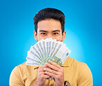 Money, winner and man cover face isolated on blue, studio background for winning, cash fan or financial loan. Lottery, bank and asian person winning bonus, budget secret or finance profit in portrait