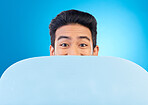 Board, peek and portrait of a man in a studio with mockup space for marketing, advertising or promotion. Excited, hide and male model with a poster mock up for design isolated by a blue background.