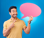 Pointing, speech bubble and thinking Asian man for communication, feedback or chat. Excited, talk and a person with a board for conversation isolated on a blue background in a studio with space