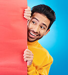 Shock, hide and young man in a studio with a wow, omg or wtf facial expression by a board with mockup. Happy, surprise and male model with sneaky face by poster with mock up space by blue background.