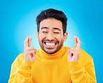 Hope, man with his fingers crossed for luck and against a blue background for competition. Praying or miracle, trust and male person with hand emoji for aspiration or wish against a backdrop.