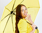 Portrait, yellow umbrella and life insurance with a woman in studio on a gray background blowing a kiss. Rain, winter fashion and smile with a happy young female model posing for cover or security