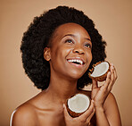 Beauty, skincare and coconut with a model black woman in studio on a brown background for natural treatment. Thinking, skin and cosmetics with a happy young female person holding fruit for oil