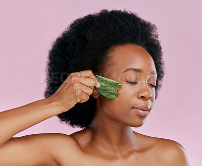 Buy stock photo Gua sha, massage and black woman with natural beauty, face care and skin glow on pink background. Female model, jade cosmetic tools and dermatology with afro hair and facial skincare in studio