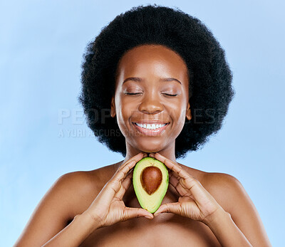 Buy stock photo Face, beauty and avocado with a black woman on a blue background in studio to detox for wellness. Skincare, smile and eyes closed with a happy young female model holding a fruit for antioxidants