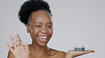 Face, product and beauty with a model black woman in studio on a gray background for skincare treatment. Portrait, wink and lotion with an attractive young female indoor to apply facial moisturizer