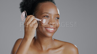 Buy stock photo Facial roller, woman and smile in face massage in skincare or beauty, health and wellness or dermatology. Happy black person, skin and cosmetics with glow, care and tool in studio by gray background