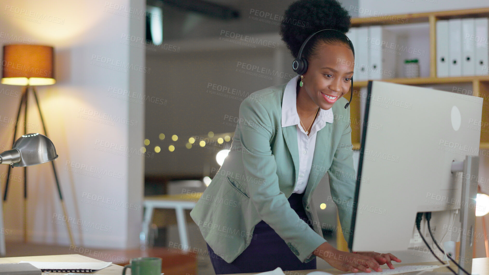 Buy stock photo African woman, call center and typing in office with microphone, night or telemarketing with contact us. Consultant, crm and tech support agent with customer service, pc and reading at help desk