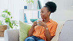 Coffee, happy and black woman relax on a sofa while laughing, watching and streaming in her home. Comic, entertainment and lady on a couch with tea, positive and chilling in a living room on day off