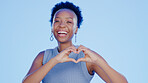 Happy, heart and face of a black woman in a studio with a positive, happiness and confident mindset. Happiness, smile and portrait of African female model with a love hand gesture by blue background.