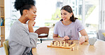 Friends, chess and board game and checkmate with the winner laughing and thinking about plan. Diversity women together at table in room happy about competition move and strategy to win on chessboard