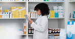 Young and focused pharmacist use her tablet to do stock taking in a modern pharmacy drugstore. Multiethnic female health professional worker or medication expert in a chemist using a digital gadget