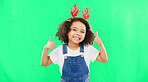 Happy, Christmas and thumbs up with girl in studio for holiday, festive and agreement. Approval, yes and like with child and deer headband on green background for satisfaction, smile and good news