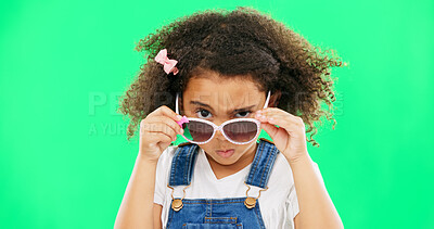 Child, portrait and sunglasses with an attitude on green screen background peeking over glasses. Black girl kid in studio for comic, funny and facial expression or mood while angry or curious