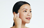 Gua sha, beauty and woman massaging face isolated on a white background in a studio. Spa, skincare and an Asian girl with a product to massage for facial relaxation, treatment and anti aging