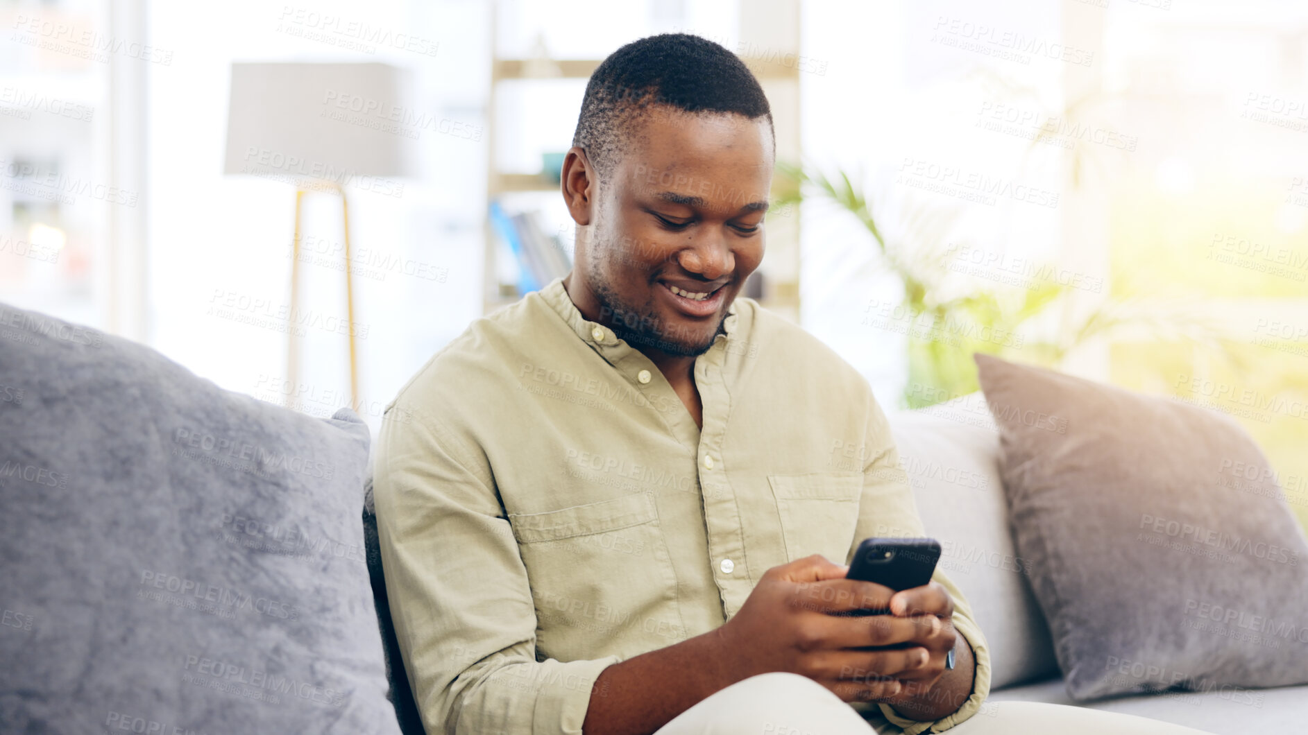 Buy stock photo Black man, phone and smile on sofa for social media, communication or networking in living room at home. Happiness, African person relaxing on couch with mobile smartphone for browsing or chatting