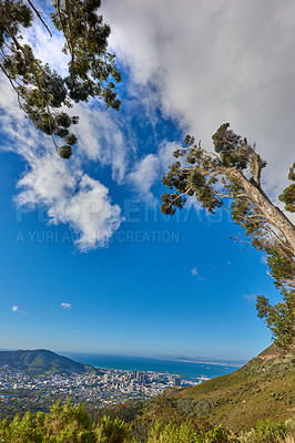 Buy stock photo Beautiful scenic view of a coastal city from a mountain peak with trees and plants against a cloudy blue sky background. Magnificent panoramic of a peaceful landscape at the sea to explore and travel