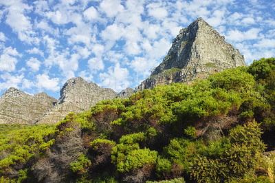 Buy stock photo Below of mountains with bushes and a blue cloudy sky background. Cloudscape and nature landscape of mountain rock outcrops with wild green plants near tourism attraction, Twelve Apostles, Cape Town