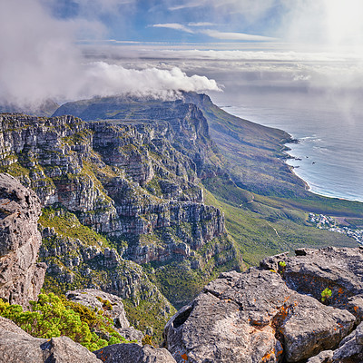 Buy stock photo Panoramic aerial nature views of clouds rolling over a mountain on the coast during summer. Copyspace scenic view of a natural environment on a coastline with rocks, plants, and greenery from above