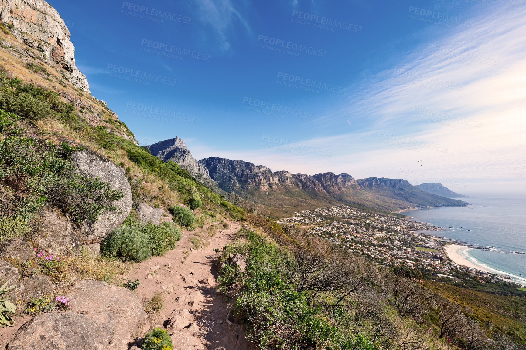 Buy stock photo Scenic coast and rocky mountain slope with a cloudy blue sky background with copy space. A rugged landscape of plants growing on a cliff by the sea with hiking trails to explore in a rocky terrain