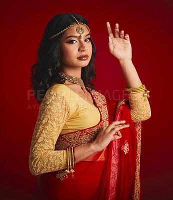Buy stock photo Portrait, beauty and Indian woman with fashion, traditional dress and luxury against a red studio background. Face, female person and model with cultural clothes, jewellery and gold with religion