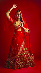 Fashion. dance and Indian woman in a traditional dress, jewellery and celebration on a red studio background. Female person, girl and model with a cultural outfit, dancing and routine with confidence