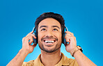 Indian man, listening and music with smile for fun in blue background with radio or podcast. Happiness, guy and headphones for songs or online streaming or entertainment in studio, spotify or media.