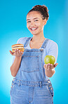 Portrait, smile and woman with burger, apple and choice in studio isolated on a blue background. Face, fruit and person with sandwich, fast food or decision for healthy diet, nutrition or wellness.
