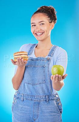 Buy stock photo Portrait, smile and woman with burger, apple and choice in studio isolated on a blue background. Face, fruit and person with sandwich, fast food or decision for healthy diet, nutrition or wellness.