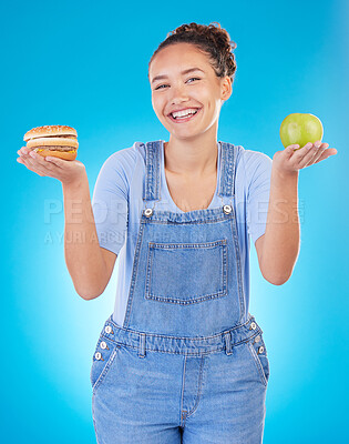 Buy stock photo Happy, portrait and woman with burger, apple and choice in studio isolated on a blue background. Smile, fruit and person with sandwich, fast food or comparison for healthy diet, nutrition or wellness