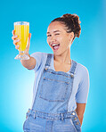 Happy woman, portrait and juice for vitamin C, diet or healthy drink against a blue studio background. Female person or model with denim fashion holding glass with organic fruit blend or breakfast