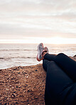 Fitness, shoes and beach in nature feeling relax with freedom outdoor sitting. Waves, ocean and water with a person and athlete taking a break from training and workout with feet in summer sun